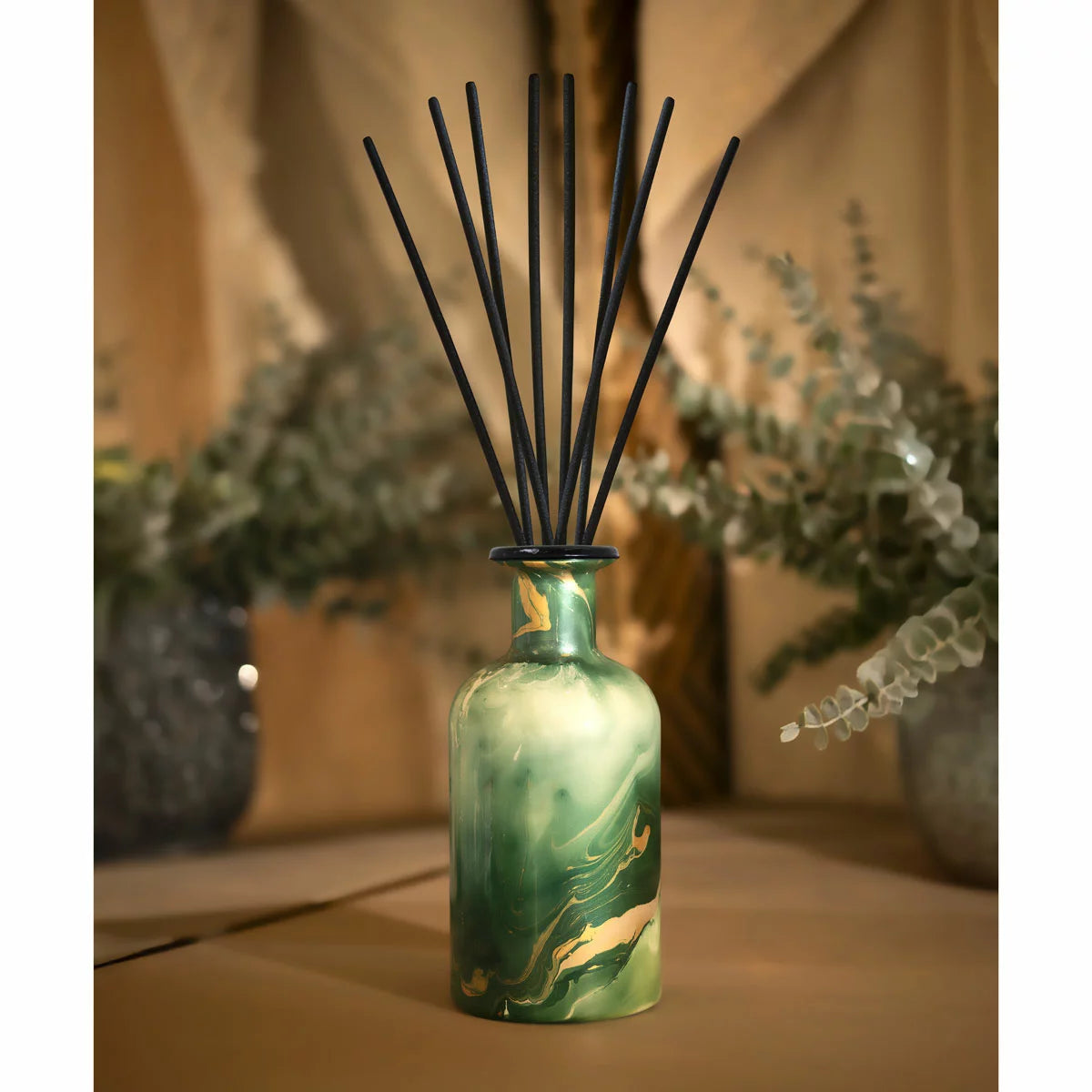 TORC Neroli & Violet green marbled reed diffuser bottle with black reeds on a wooden surface with plants in the background