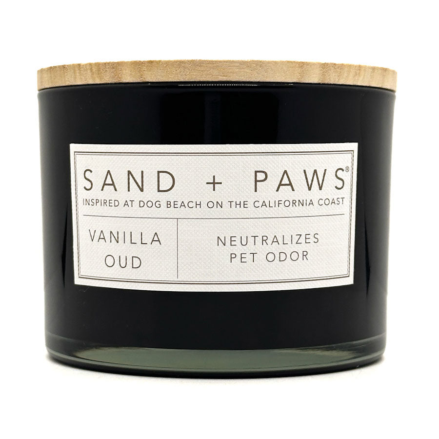 Vanilla Oud Black candle with a wooden lid labeled 'Sand + Paws' on a white background