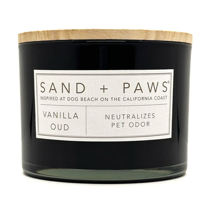 Vanilla Oud Black candle with a wooden lid labeled 'Sand + Paws' on a white background