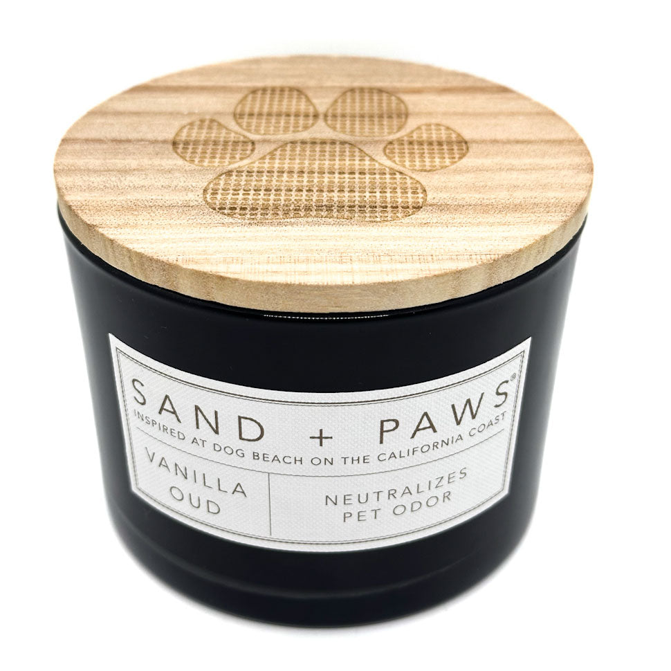 Vanilla Oud Black candle with wooden lid featuring a paw print design, labeled 'Sand + Paws'.