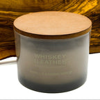 Candle labeled 'Whiskey Leather' Vanilla Sandalwood with a wooden lid against a wooden background