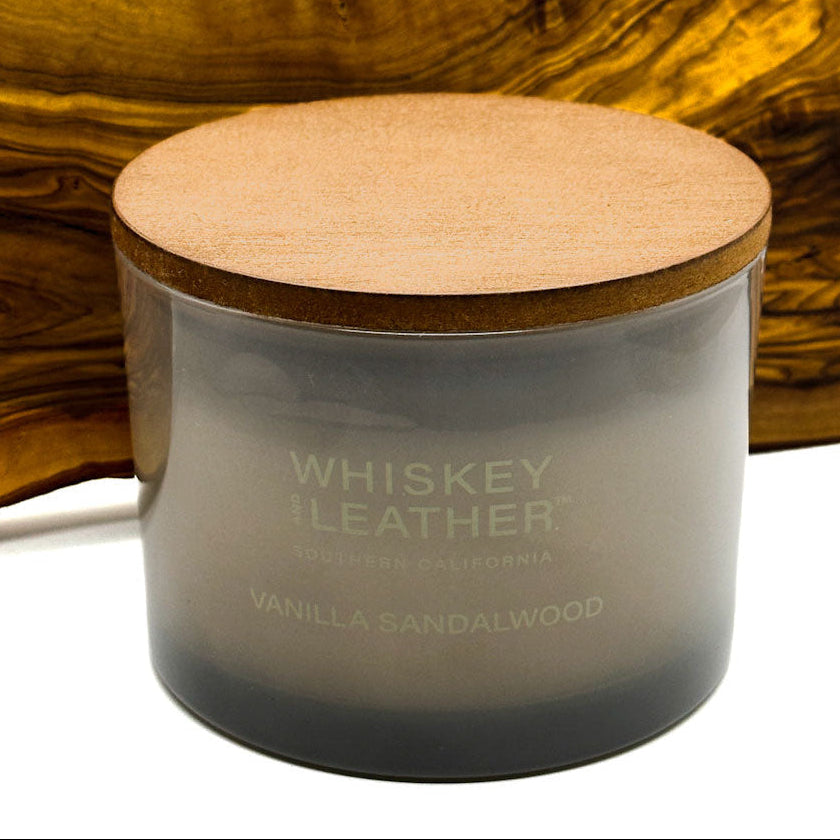 Candle labeled 'Whiskey Leather' Vanilla Sandalwood with a wooden lid against a wooden background