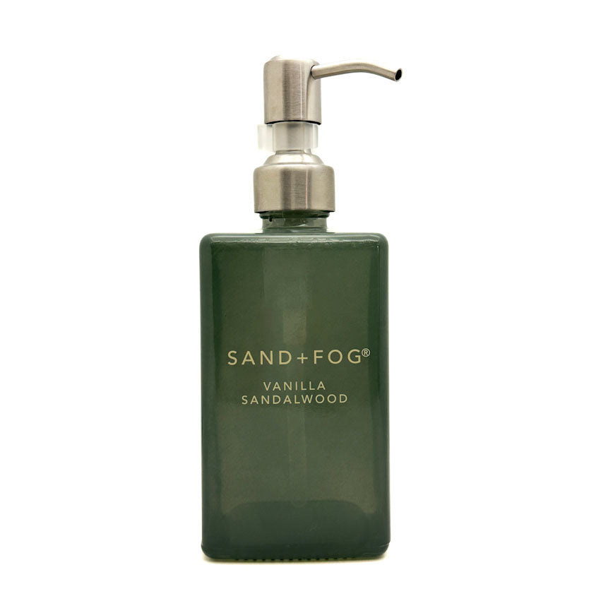 A dark green rectangular pump bottle with a silver metal dispenser, labeled 'SAND+FOG VANILLA SANDALWOOD', on a plain white background.