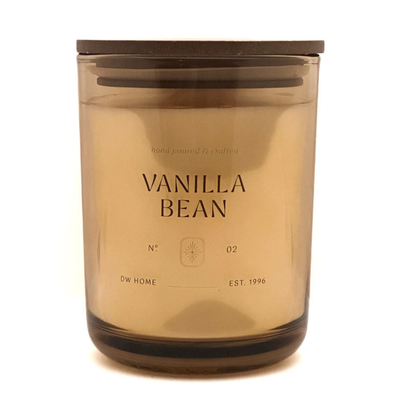 A DW Home jar candle with a dark brown lid and translucent amber glass, featuring the text 'VANILLA BEAN' on the front, set against a plain white background.