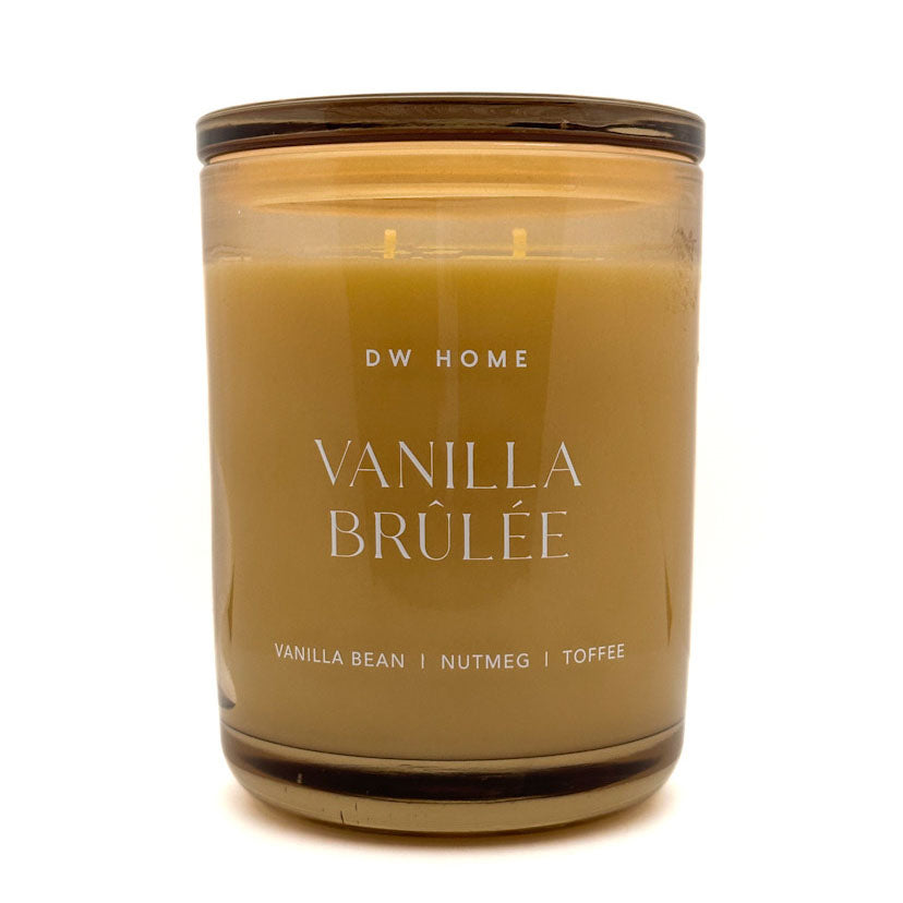An Extra Large double-wick candle in an amber glass jar with a dark brown lid, labeled 'DW HOME VANILLA BRÚLÉE' on a white background.