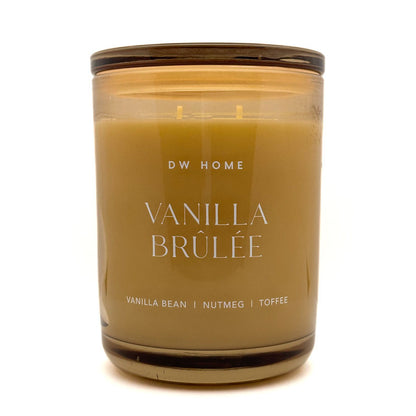 An Extra Large double-wick candle in an amber glass jar with a dark brown lid, labeled 'DW HOME VANILLA BRÚLÉE' on a white background.