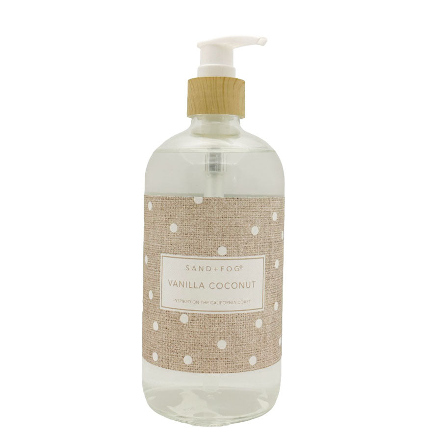 A clear pump bottle of Sand+Fog Vanilla Coconut hand wash with a beige burlap-style label featuring white polka dots and a white pump dispenser.