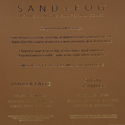 A close-up of a brown cardboard product label for Sand + Fog fragrance oil, showing text for Vanilla Latte and Sugar & Amber scents.