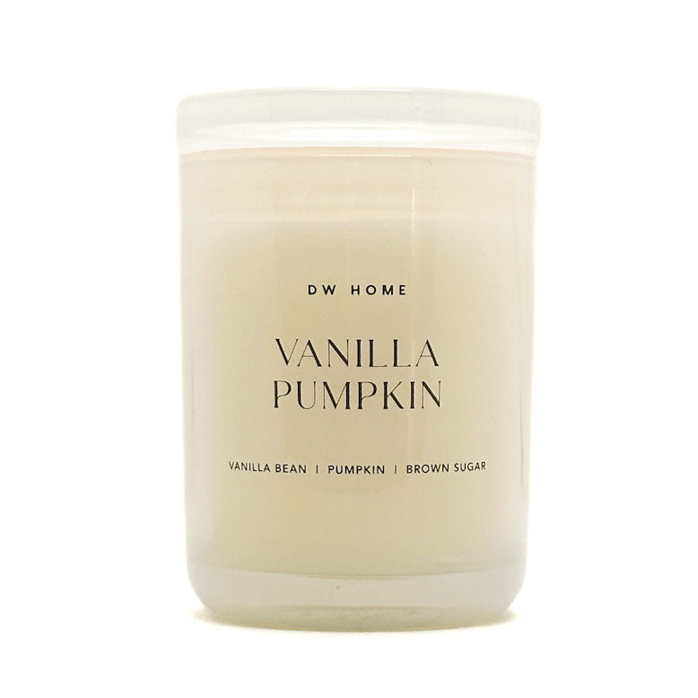 A frosted glass jar candle with creamy off-white wax, featuring a white lid and black text that reads 'DW HOME VANILLA PUMPKIN' on the front label.