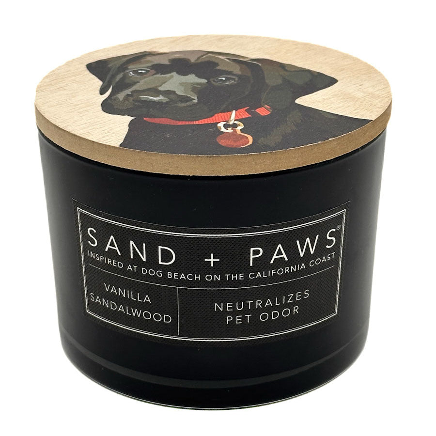 Vanilla Sandalwood black candle with a dog illustration on the lid, labeled 'Sand + Paws'.