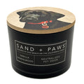Vanilla Sandalwood black candle with a dog illustration on the lid, labeled 'Sand + Paws'.