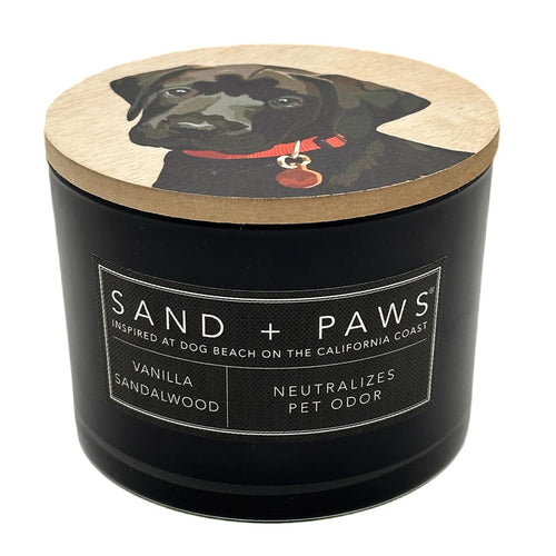 Vanilla Sandalwood black candle with a dog illustration on the lid, labeled 'Sand + Paws'.