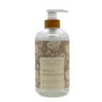 A 64 fl oz clear plastic bottle of Sand + Fog Vanilla Sandalwood scented hand soap with a white pump dispenser and a brown floral patterned label.