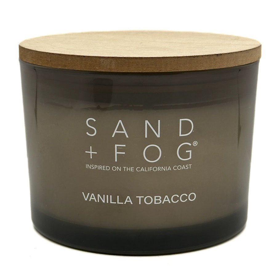 Candle with wooden lid labeled 'Sand + Fog Vanilla Tobacco' on a white background