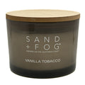 Candle with wooden lid labeled 'Sand + Fog Vanilla Tobacco' on a white background