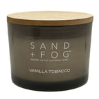 Candle with wooden lid labeled 'Sand + Fog Vanilla Tobacco' on a white background