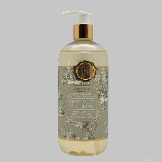 A bottle of HOpificio Italian White Musk hand wash, featuring a clear bottle with pale yellow liquid, a white pump dispenser, a gold collar, and a grey floral label with gold accents, set against a solid grey background.