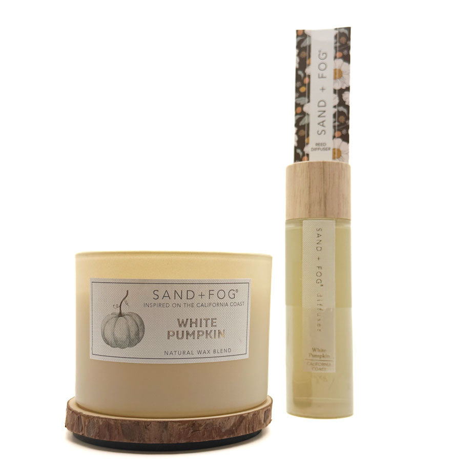 A Sand + Fog White Pumpkin natural wax candle in a cream-colored jar with a wood-grain base, shown next to its matching 10ml travel spray bottle with a light wood cap on a white background.
