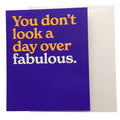 A square greeting card with a deep purple front and a cream envelope behind it. The card features the humorous phrase 'You don't look a day over fabulous.