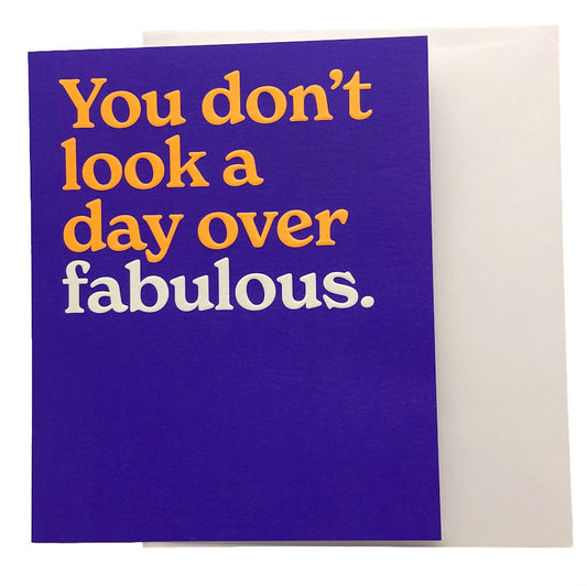 A square greeting card with a deep purple front and a cream envelope behind it. The card features the humorous phrase 'You don't look a day over fabulous.